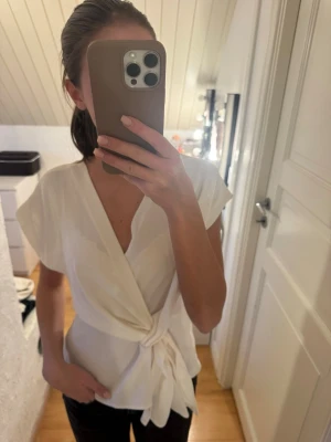 Vit omlottblus med knyt från Zara - Snygg vit omlottblus från Zara med knyt framtill. Blusen har korta ärmar och djup v-ringning. 