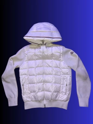 Vit Cardigang från Moncler - ÄKTA:  Snygg vit pufferjacka från Moncler med quiltad front och huva. Jackan har stickade ärmar och muddar, dragkedja framtill och två fickor med dragkedja. Moncler-logga på ärmen och diskret text på huvan. Perfekt för kalla vinterdagar.