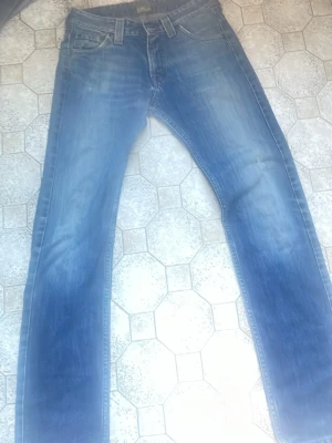 Blå raka jeans från Lee - Säljer ett par klassiska blå jeans från Lee med raka ben och snyggt slitna detaljer. Jeansen har fem fickor, normal midja och Lee-logga på bakfickan samt bak i linningen. Perfekta till vardagslooken och passar till det mesta.