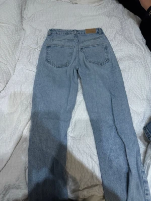  ljusblå raka jeans - Klassiska ljusblå jeans från Levi's med rak passform och hög midja. Jeansen har fem fickor, bälteshällor och en patch med Levi's-loggan bak i midjan. Tillverkade i slitstark denim, perfekta för en avslappnad och tidlös stil.