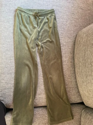 Olivgröna velour mjukisbyxor - Säljer ett par olivgröna mjukisbyxor i mjuk velour med lite flair ben och dragsko i midjan. Byxorna har två bakfickor och en avslappnad passform som är perfekt för chill dagar. Inga synliga loggor eller märken.