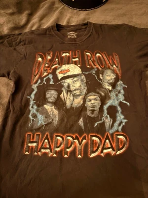 Death Row Happy Dad t-shirt svart - Svart t-shirt från Death Row med stort tryck på framsidan där det står 'Death Row' och 'Happy Dad' samt motiv av kända rappare och blå blixtar. Klassisk passform och rund hals. Perfekt för dig som gillar streetwear och hiphop.