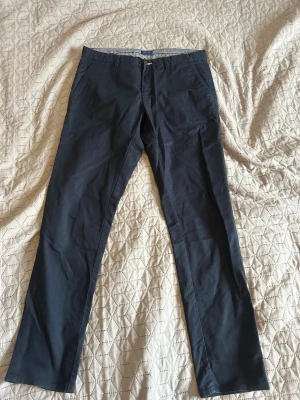 Mörkblå chinos från H&M - Snygga mörkblå chinos från Gant med raka ben och klassisk passform. Byxorna har två sidofickor fram och två bakfickor, perfekta för en clean och stilren look. Tillverkade i mjuk bomull för skön komfort hela dagen. Saknas en knapp på bakfickan. 