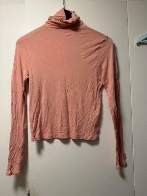 Ljusrosa polotopp från H&M Divided - Säljer en ljusrosa polotopp från H&M Divided. Toppen har lång ärm, croppad passform och är tillverkad i mjuk bomullsmix. Perfekt att styla med jeans eller kjol för en enkel och trendig look.