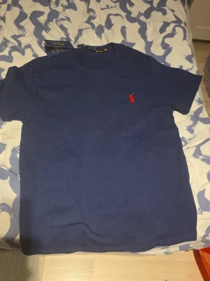 Marinblå t-shirt från Polo Ralph Lauren - Klassisk marinblå t-shirt från Polo Ralph Lauren med röd broderad logga på bröstet. Skön passform och rund halsringning. Perfekt basic-plagg till garderoben.