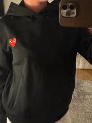Svart hoodie Comme des Garçons Play - Svart hoodie från Comme des Garçons Play med den ikoniska röda hjärtloggan med ögon på bröstet. 