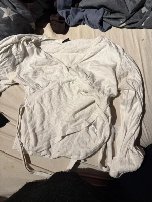 Vit omlottopp med långa ärmar - Säljer en vit omlottopp med långa ärmar och knytband i midjan. Toppen har en v-ringad design och är tillverkad i ett mjukt, ribbat material. Perfekt för dig som gillar stilrena och enkla plagg.