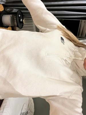 Vit fleece-tröja från The North Face - Säljer en vit fleece med halv dragkedja och hög krage och kortare variant från The North Face. Materialet är mjukt och värmande.