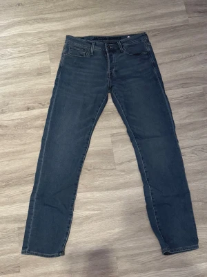 Mörkblå jeans från Jack & Jones - Snygga mörkblå jeans från Jack & Jones med klassisk femficksdesign och raka ben. Jeansen har normal midja och är tillverkade i ett mjukt denimtyg med lite stretch för extra komfort. Storlek 32/34