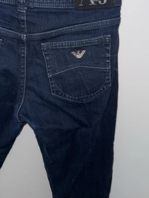 Mörkblå vintage jeans från Armani Jeans - Snygga mörkblå jeans från Armani Jeans med klassisk femficksdesign och silverfärgad logga på bakfickan. Jeansen har raka ben och är tillverkade i ett mjukt denimtyg som sitter skönt. Perfekta för en trendig och avslappnad look.