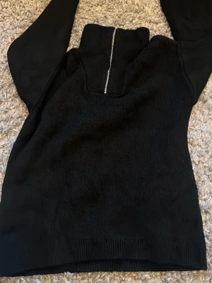 Svart stickad tröja med dragkedja ONLY - Snygg svart stickad tröja från ONLY med hög krage och silverfärgad dragkedja framtill. Tröjan har lång ärm och ribbade muddar vid ärmslut och nederkant. Perfekt för kyliga dagar och enkel att matcha med olika outfits.