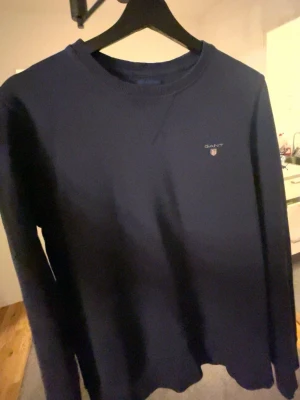 Mörkblå sweatshirt från GANT - Klassisk mörkblå sweatshirt från GANT med rund halsringning och diskret logga broderad på bröstet. Tröjan har långa ärmar och är tillverkad i mjukt material som passar perfekt till jeans eller chinos.