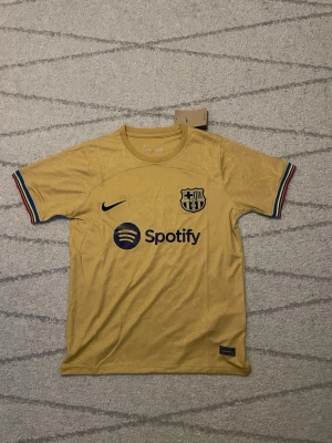 FC Barcelona gul matchtröja Pedri #8 - Gul FC Barcelona matchtröja från Nike med Pedri #8 på ryggen. Tröjan har klubbmärke, Nike-logga och Spotify-tryck framtill samt UNHCR-logga bak. Ärmarna har ränder i klubbens färger. Perfekt för fotbollsfans!