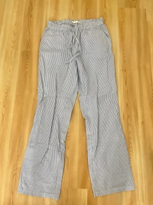 Randiga linnebyxor - Snygga linnebyxor med smala vita och blå ränder. Byxorna har rak passform och elastisk midja. Perfekta för en avslappnad och trendig look. Tillverkade i ett lätt och luftigt linnematerial. Det finns en liten fläck på midjan men som knappt syns.