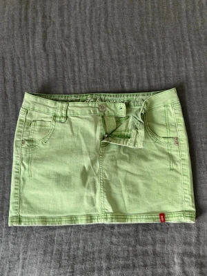 Ljusgrön jeanskjol från Esprit - Trendig ljusgrön jeanskjol från Lee med klassisk femficksmodell, bälteshällor och knappgylf. Kjolen är kort och har en rak passform i stretchigt denimtyg. Perfekt för dig som vill ha en färgklick i garderoben.