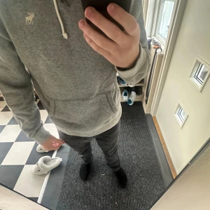 Grå hoodie Abercrombie & Fitch M - Säljer en grå hoodie från Abercrombie & Fitch i storlek M. Tröjan har huva med snörning, magficka och ett litet broderat älg-logo på bröstet. Mjuk insida och långärmad, perfekt för chill dagar. Passformen är normal och materialet känns som bomull och polyester.