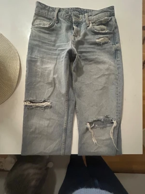 Ljusblå slitna jeans Zara st 34 - Säljer ett par ljusblå  jeans från Zara med flera slitningar och hål på både knän och fickor. 