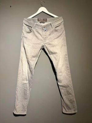Ljusgrå jeans från Jacob Cohën - Snygga ljusgrå jeans från Jacob Cohën Jeans med klassisk femficksmodell och raka ben. Jeansen har ljusblå detaljer och är tillverkade i mjuk denim. Perfekta för en avslappnad och trendig stil. Jeansen är skräddarsydda i Italienska fabriker.