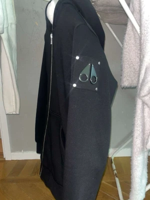 Svart hoodie från Moose Knuckles - Säljer en svart hoodie från Moose Knuckles med dragkedja, köpt för 3995 kr från kidsbrandstory, storlek 176. 
