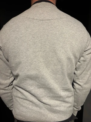 Grå sweatshirt från Stone Island - Säljer en stilren grå sweatshirt från Stone Island med den klassiska svarta patchen och gult broderat märke på ärmen. Tröjan har rund halsringning och är tillverkad i mjukt bomullsmaterial. Perfekt för dig som gillar streetwear och vill ha något bekvämt och snyggt. Den har en lapp med certilogo samt en nfc tag som man kan skanna, då tas man till stone Island hemsidan. Är andvänt men synns knappt. Passar större S och Vanlig M. Det är bara att fråga om fler bilder mm PRIS KAN DISKUTERAS 