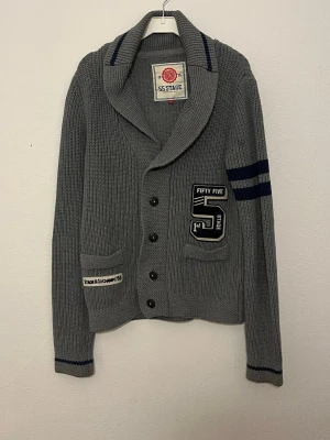 Cardigan  - Hej nu säljer vi denna grymt feta 55 stage cardigan i en stilren grå färg som lätt gör att klä sig bra i. Skicket 9/10 inga defekter. Storleken: M. Bröstlängd: 45cm. Midjalängd: 45cm. Längd:60cm. Armlängd: 65cm. För fler frågor hör gärna av er så hörs vi!