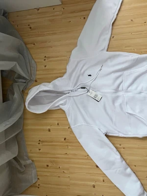 Vit hoodie från Ralph Lauren - Snygg vit hoodie från Ralph Lauren med dragkedja framtill och klassisk huva. Hoodien har det ikoniska lilla Polo-logotypen broderad på bröstet och ribbade muddar vid ärmar och nederkant. Perfekt för en clean och stilren look. Vissa vad du har att erbjuda så kanske vi kan diskutera fram ett pris där både jag och du är nöjda 
