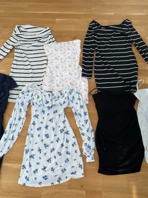 7 trendiga klänningar i olika stilar - Paket med 7 klänningar i olika färger och mönster. Inkluderar en marinblå spetsklänning, en vit klänning med blå blommor och långa ärmar, en vit klänning med röda blommor, en svart ribbad klänning, samt två randiga klänningar i svart och vitt. Perfekt för dig som vill variera din stil.