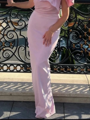 Ljusrosa långklänning med rosett - Elegant ljusrosa långklänning med en axel och stor dekorativ rosett på axeln. Klänningen har figurnära passform och är tillverkad i ett slätt material som ger en lyxig känsla. Perfekt för speciella tillfällen när du vill sticka ut. Kolla min profil för fler plagg! 🥰