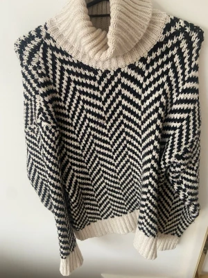 Svartvit stickad polotröja - Snygg stickad polotröja i svartvitt sicksackmönster. Tröjan har en hög, ribbstickad polokrage.