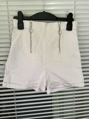 Vita högmidjade shorts med dragkedjor storlek: XS - Snygga vita högmidjade shorts med två silverfärgade dragkedjor framtill och uppvikta benslut. Perfekta för varma dagar och enkel att matcha med olika toppar. Stilsäker och modern design.