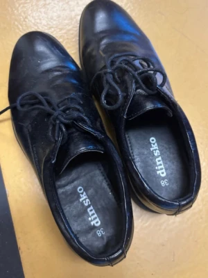 Svarta loafers från Din Sko, strl 38 - Klassiska svarta loafers från Din Sko i storlek 38. Skorna har snörning framtill och är tillverkade i ett glansigt material som ger en stilren look. Perfekta för dig som vill ha en enkel men snygg sko till vardagslooken.