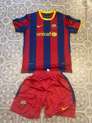 Barcelona tröja - Säljer ett FC Barcelona matchställ från Nike med klassiska blå och röda vertikala ränder. Tröjan är aldrig använd och är storlek 28. klubbmärke och Unicef-logga på bröstet. Shortsen är röda och medföljer. Storlek 28 motsvarar ungefär storlek 152. Tröjan är 100% polyester, och säljs därför billigare. Fraktar samma dag!✅🚛