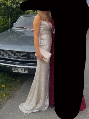 Glittrig champagne balklänning - Säljer en glittrig champagnefärgad balklänning med v-ringning och smala axelband. Klänningen har en snygg slits på sidan och är täckt av paljetter som ger ett riktigt statement-utseende. Perfekt för bal eller student! Den är använd 2 gånger med jättebra skick! Pris går att diskuteras