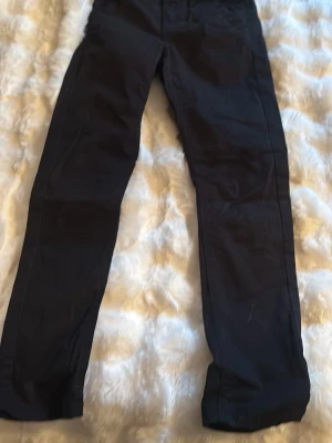 Svarta raka byxor - Svarta byxor med rak passform och klassisk design. Byxorna har normal midja och är tillverkade i ett slätt tyg som ger en stilren look. Perfekta för dig som gillar enkel och tidlös stil.