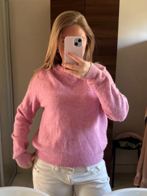 Rosa stickad tröja med rund hals - Mysig rosa stickad tröja med rund halsringning och långa ärmar. Tröjan har ribbstickade muddar vid ärmslut och nederkant. Perfekt för kyliga dagar och enkel att matcha med olika outfits.