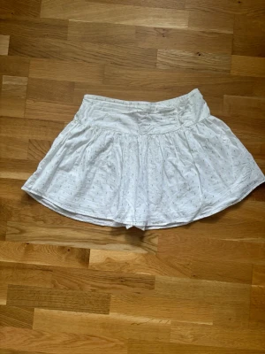 Vit kortkjol från Gina Tricot - Söt vit kortkjol från Gina Tricot med diskret mönster. Kjolen har en bred resår i midjan och är gjord i ett lätt och luftigt bomullstyg, perfekt för varma dagar. Passar dig som gillar en enkel men ändå detaljerad stil.
