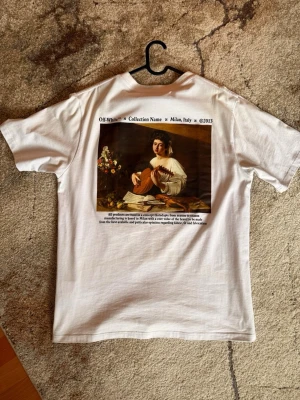 Vit Off-White t-shirt med tryck - Vit t-shirt från Off-White med svart logga på bröstet och stort konstmotiv på ryggen. Klassisk passform och rund halsringning. Tillverkad i mjuk bomull som känns skön mot huden. Perfekt för dig som gillar streetwear och unika prints.