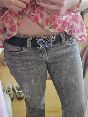 Svart bälte med blå fjärilsspänne - Snyggt svart bälte med ett stort, dekorativt fjärilsspänne i silverfärg och blå stenar. Perfekt accessoar för att lyfta din outfit med en unik detalj. Jag fick ärva detta från min mamma så jag vet tyvärr inte märket. Det är använt men fortfarande i bra skick. 
