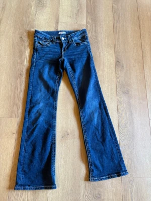 Mörkblå bootcut jeans - Säljer ett par mörkblå bootcut jeans med klassiska fem fickor och kontrastsömmar. Jeansen har normal midja och utsvängda ben. Perfekta för dig som gillar en retroinspirerad look. Materialet är denim i bomull.