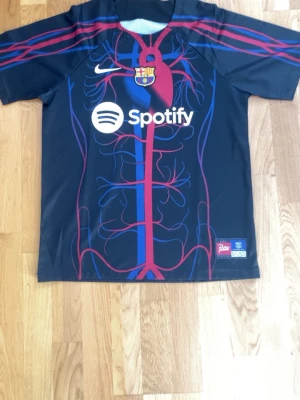 Barcelona Nike matchtröja anatomiskt tryck - Unik Barcelona matchtröja från Nike med anatomiskt inspirerat tryck i rött och blått på framsidan. Tröjan har klubbmärke, Nike-logga och Spotify som sponsor. Tillverkad i lätt och ventilerande material, perfekt för fotboll eller träning.