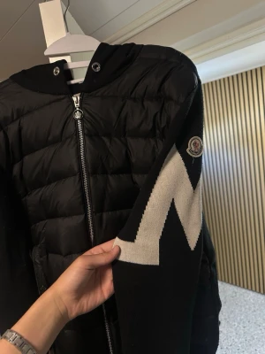 Moncler cardigan  - Svart moncler cardigan, den har både nfc scan och qr kod scan. Den är dock lite sönder nere vid höger armhålan men det är något som inte syns när man har på jackan.man kan också enkelt sy ihop och den.