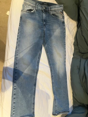 Ljusblå raka jeans från Replay - Snygga ljusblå jeans från Replay med raka ben och klassisk femficksmodell. Jeansen har en tvättad look med slitningar och är tillverkade i mjukt denimtyg. Perfekta för en avslappnad och trendig stil.
