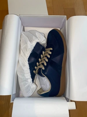 Mörkblå Margiela Gats - Snygga marinblå sneakers med beige snörning och gummisula. Skorna har en mix av mocka och slätt läder, vilket ger en schysst kontrast. Perfekta för dig som gillar klassisk men ändå trendig stil. Tidlös design som funkar till det mesta.