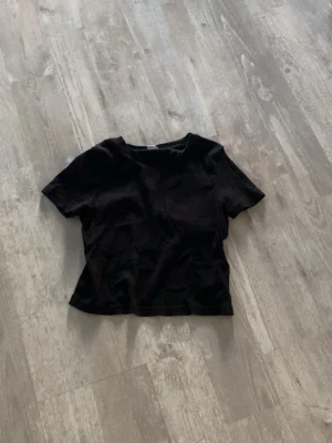 Svart t-shirt från Lindex - En enkel ribbad svart t-shirt från Lindex med rund hals och korta ärmar. Perfekt basplagg som passar till allt och har en klassisk passform. Tillverkad i mjuk bomull för skön känsla hela dagen.