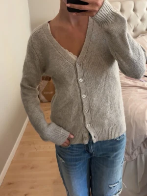 Beige/grå stickad kofta med knappar - Mysig beige stickad kofta med v-ringning från zara. Koftan har långa ärmar och ribbade muddar vid ärmslut och nederkant. Perfekt att slänga över en topp eller linne💝🤍