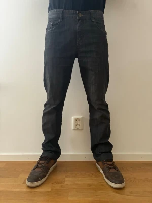 Burberry jeans - Säljer ett par mörkgrå jeans från Burberry med rak passform och klassisk femficksdesign. Jeansen har normal midja, bälteshällor och subtila slitningar för en avslappnad look. Perfekta för dig som gillar streetwear och vill ha en tidlös stil.