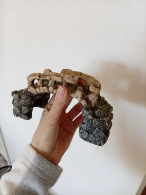 Dekorativ akvariebro i konststen - Säljer en cool dekoration till akvarium i form av en gammal stenbro med detaljer som ser ut som mossa och slitna stenar. Bron är gjord av konstmaterial och har en naturlig look med grå, brun och grön färg. Perfekt för att skapa en mysig miljö till fiskarna.