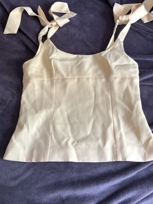 Gul linnetopp med knytband - Snygg Gul linnetopp med breda axelband som knyts i rosetter. Toppen har en enkel och stilren design med slät yta och lätt figursydd passform. Perfekt för att skapa en fräsch och trendig look.