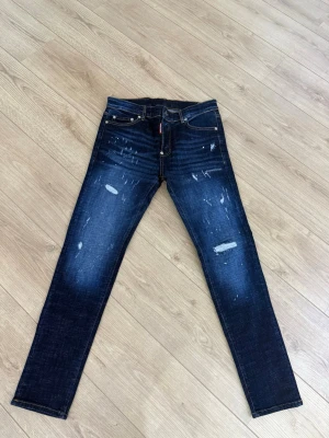 DSQUARED2 jeans - Snygga mörkblå jeans från DSQUARED2 med slitna detaljer och klassisk femficksdesign. Jeansen har en gul patch med logga bak i midjan och är tillverkade i stretchigt denim för en bekväm passform.