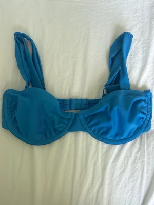 Blå bikiniöverdel - Snygg blå bikiniöverdel med breda axelband och bygel för extra stöd. Klassisk modell med enkel knäppning bak och slät design utan mönster. Perfekt för strandhäng eller pooldagar. Har tvättat den men aldrig använt. Från NA-KD